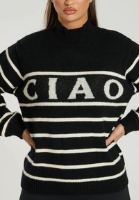 Gestreifter schwarz-weißer Strickpullover mit Stehkragen, versehen mit dem Text "CIAO" und gerippten Bündchen, Saum und seitlichen Taschen. Weiche Textur.