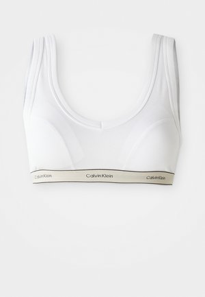 Bijela sportska grudnjak Calvin Klein s širokim trakama i elastičnim pojasom na kojem je ime brenda ispisano crnom bojom na bež pozadini.