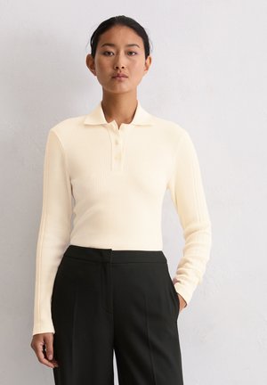 Long-sleeve, ribbed polo top in cream, featuring a collar and a button placket. Paired with high-waisted black trousers.