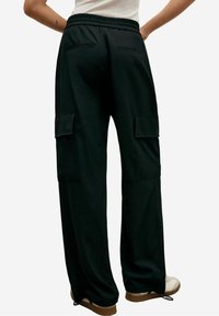 Personne portant un pantalon cargo noir ample avec taille élastique et poches à rabat, associé à des baskets blanches, vue de dos.