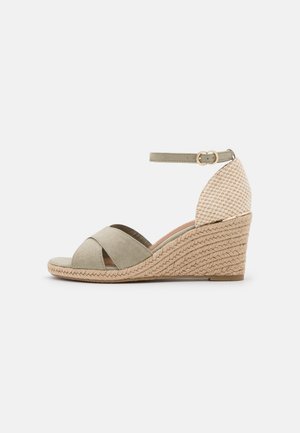 Sandale compensée beige avec un dos texturé, des brides en daim croisées, une sangle de cheville réglable et un semelle intermédiaire en jute tissé.