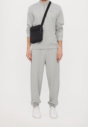 Šedý bavlněný teplákový komplet s dlouhými rukávy a zipem, doplněný o bílé tenisky a černou crossbody tašku se zipy a popruhy.