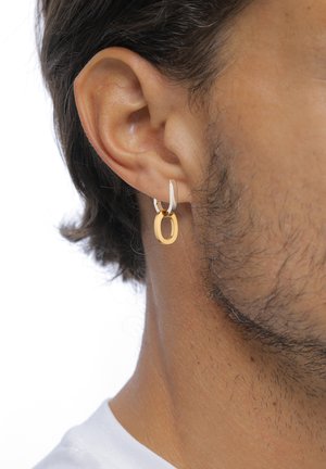 Boucle d'oreille en or et argent avec un design ovale, mettant en valeur une finition brillante et une surface texturée, portée sur une oreille modélisée.