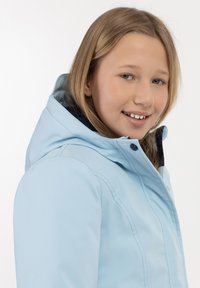 Světle modrá voděodolná bunda s kapucí, s zipovým uzavřením, kontrastní tmavou podšívkou a viditelnými švy. Hladká textura.