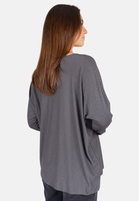 Locker sitzendes Langarmshirt aus dunkelgrauem Stoff. Weiche Textur mit rundem Ausschnitt und überschnittenen Schultern, mit seitlichen Schlitzen.