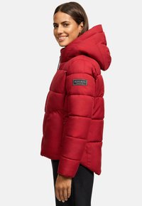 Red puffer jacket with a hood, quilted design, and branded patch. Made of smooth material with a relaxed fit and pockets.