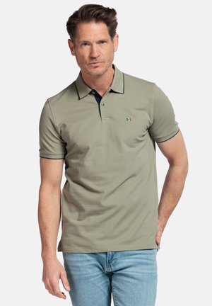 Khaki poloshirt met een donkere kraag en subtiel logo. Gemaakt van zachte stof, voorzien van korte mouwen en een klassieke pasvorm, gecombineerd met lichtblauwe jeans.