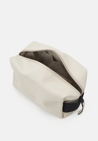 Beige vanntett toalettveske med glidelås; har et elegant design og lerret-lignende tekstur; inkluderer svarte aksentdetaljer.