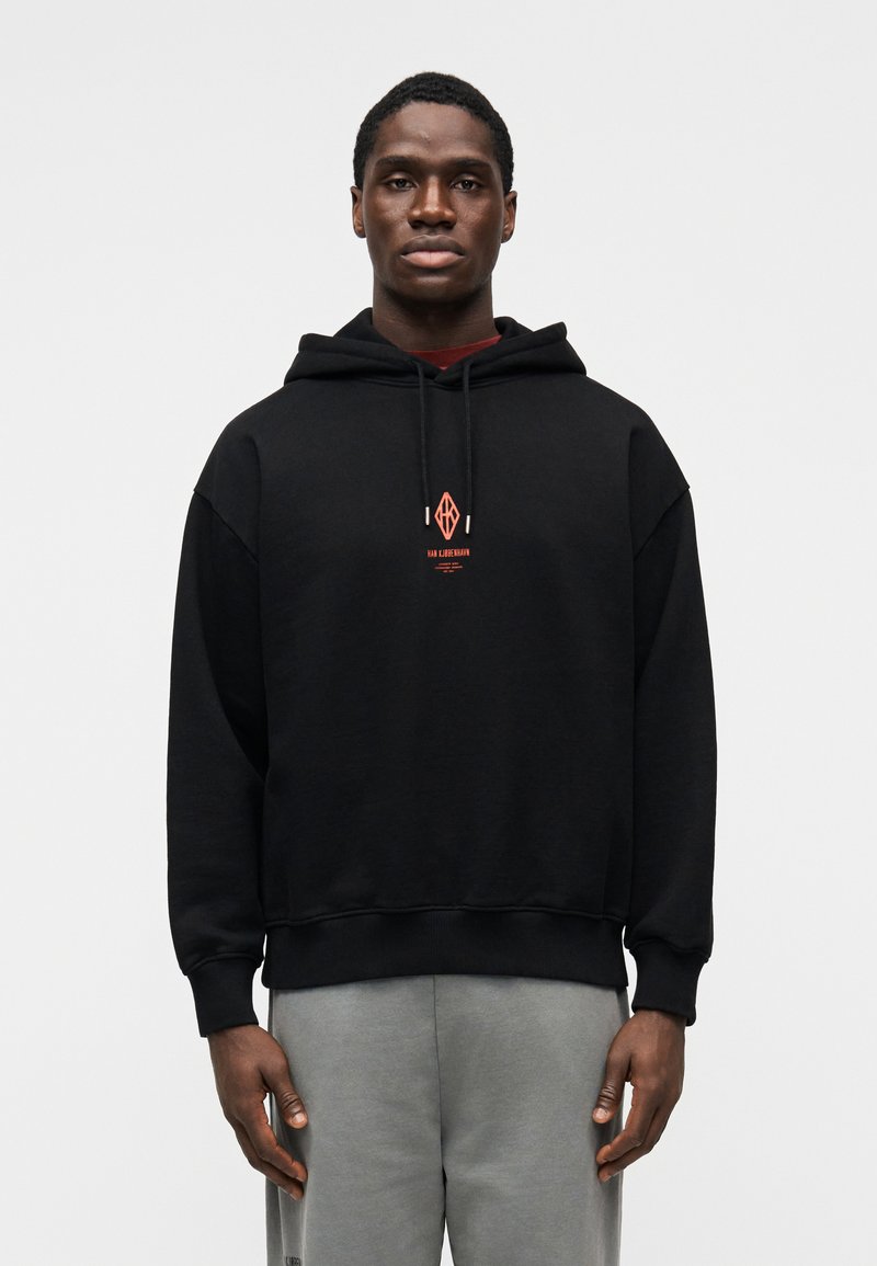 Juodas gobtuvuotas sportinis megztinis laisvo kirpimo, ant krūtinės raudonas grafiškas logotipas. Minkšta medžiaga, ribuoti rankogaliai ir juosmuo.