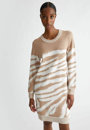 Abito lavorato a maglia in beige con motivo a strisce zebrate bianche, scollatura a girocollo e polsi a coste. Texture morbida con leggera lucentezza, accentuata da un piccolo logo.