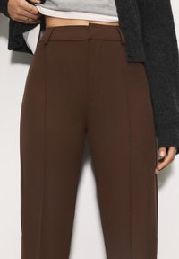 Bruine op maat gemaakte broeken met een gladde textuur, voorzien van een platte voorkant, zijzakken en een hoge tailleband, aangevuld met een donkergrijze cardigan.