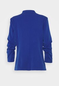 Blazer bleu à manches longues avec manches froncées, coupe ajustée et col court, vu de dos sur un fond blanc uni.