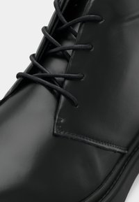Černá kožená bota s hladkým, lesklým povrchem, standardním šněrovacím systémem a šitými akcenty podél okraje.