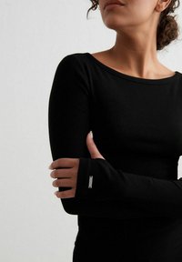 Crna majica dugih rukava s rebrastom teksturom, s pripijenim manžetama i malim metalnim akcentom na rukavu. Jednostavan okrugli izrez.