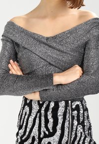 Top a spalle scoperte con maniche lunghe in tessuto metallico argento con un design incrociato, abbinato a una gonna nera con un motivo zebra argentato.