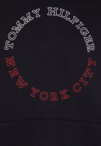 Felpa nera con grafica circolare. Il testo in bianco e rosso recita "TOMMY HILFIGER" e "NEW YORK CITY". Texture liscia, maniche raglan.