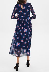 Vestido floral azul marino con mangas largas de organza, con rosas rosas y detalles en verde. La parte posterior tiene un escote en forma de llave y un dobladillo con forma de concha.