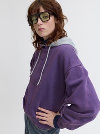 Μωβ φούτερ με γκρι κουκούλα, κορδόνια και ραμμένα μανίκια, συνδυασμένο με υπερμεγέθη πράσινα γυαλιά ηλίου. Άνετη εφαρμογή, μαλακή υφή.