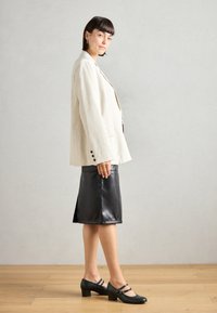 White pinstriped blazer over a black leather skirt, paired with black heeled shoes featuring two straps. Smooth texture and tailored fit.