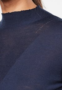 Top de cuello alto acanalado en color azul marino con un tejido texturizado, que presenta un escote con volantes y un detalle diagonal en el pecho.