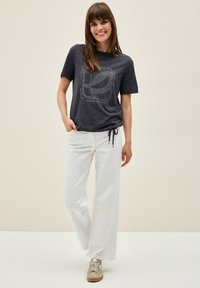 Dark gray cotton t-shirt with a rounded neckline and short sleeves, featuring a white printed design. Paired with white wide-leg pants and sneakers.