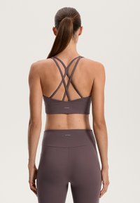 Sportski grudnjak u prigušenoj ljubičastoj boji, s preklopnim trakama na leđima i logotipom na rubu. Glatka tekstura i prilagođeni dizajn.