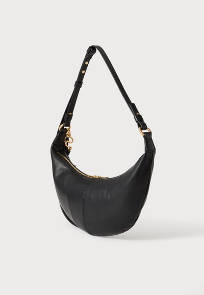 Sac d'épaule en cuir noir en forme de croissant avec bandoulière ajustable et fermeture éclair et fermoir en métal doré sur fond blanc.