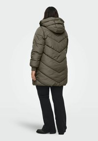 Olive green puffer coat with a hood, featuring a chevron pattern and elastic cuffs. Worn over black pants and black shoes.