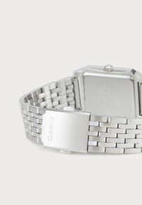 Montre en acier inoxydable argenté avec un bracelet texturé en maillons. Le boîtier carré présente un design minimaliste et un fermoir à bouton-poussoir marqué "CASIO."