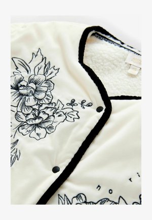 White fleece jacket with black floral embroidery. Features a black trim and snap closures. Soft texture and detailed floral design.