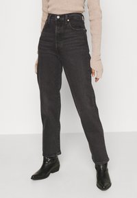 Jeans de denim negros de cintura alta con un diseño de pierna recta, que cuentan con bolsillos frontales y un ligero desvanecido. Combinados con botas de tobillo negras de punta.