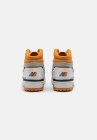Une paire de baskets New Balance blanches et oranges vues de l'arrière sur un fond blanc uni.