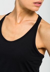 Černý bezramenní sportovní top s kulatým výstřihem. Vyrobený z měkké, elastické tkaniny, která zvýrazňuje ramena a oblast klíční kosti.