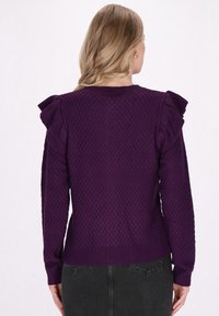 Purple knitted sweater featuring textured pattern, long sleeves, and ruffled accents on shoulders. Ribbed cuffs and hem complete the design.