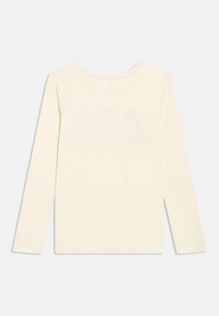Μπλούζα μακρυμάνικη σε κρεμ απόχρωση με στρογγυλή λαιμόκοψη, εμφανίζεται από πίσω σε απλό ανοιχτό γκρι φόντο.