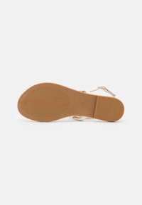 Sandal featuring a smooth, shiny silver upper with adjustable straps, and a textured, light brown rubber sole for grip.