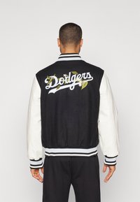 Svart og hvitt varsity-jakke med brodert "Dodgers"-logo og blomsterdetaljer, ribbestrikkede mansjetter og kant, med ullkropp og lærermte.