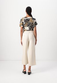 Haut à manches courtes avec un motif de feuilles en crème, noir et or ; associé à un pantalon large beige clair ; talons noirs.