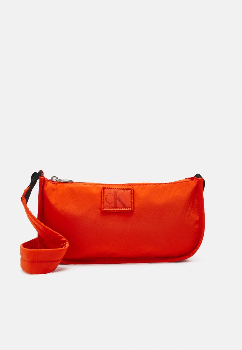 Pomarańczowa nylonowa torba na ramię Calvin Klein z zamkiem błyskawicznym, materiałowym paskiem i tłoczonym logo. Kompaktowy, prostokątny kształt. Gładka faktura.