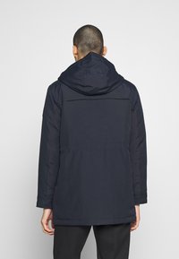 Mörkblå isolerad jacka med huva, med en slät yta, långa ärmar och rak fåll. Bakvy visar detaljer på axelsömmarna.