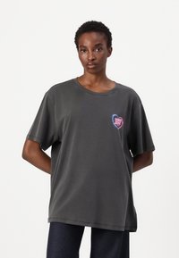 T-shirt oversize grigio scuro in cotone con collo rotondo e maniche corte, caratterizzato da una grafica colorata a forma di cuore sul petto.