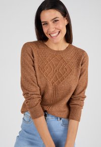 Pullover marrone a maglia con motivo a diamante e punti testurizzati. Collo rotondo e polsini a coste. Abbinato a jeans azzurri chiari.