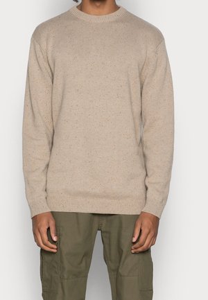 Beige knit sweater with ribbed crew neck, long sleeves, and a textured fabric pattern, paired with olive green cargo pants.
