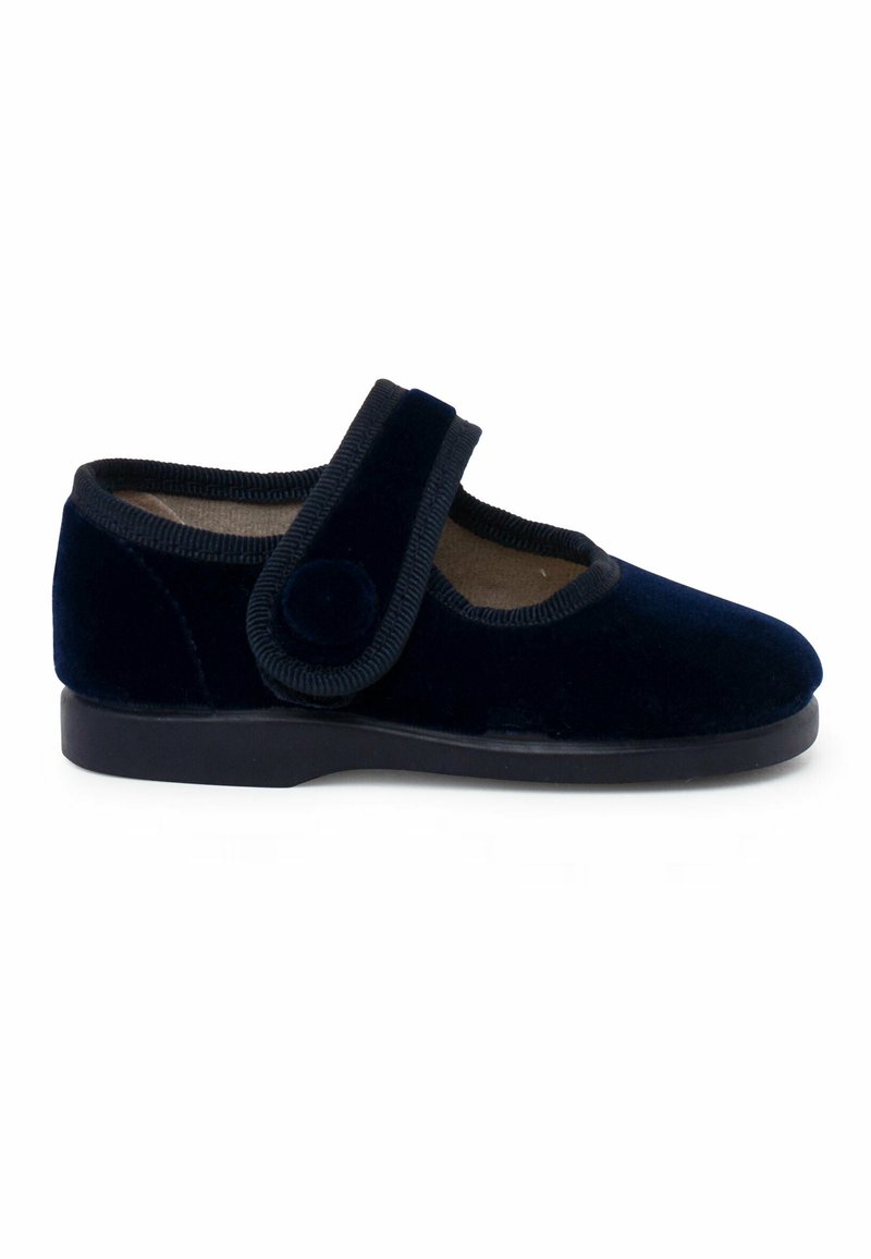 Zapato de terciopelo azul marino con puntera redondeada, suela negra plana y una amplia correa de velcro con un acento circular. Textura suave con un detalle mínimo.
