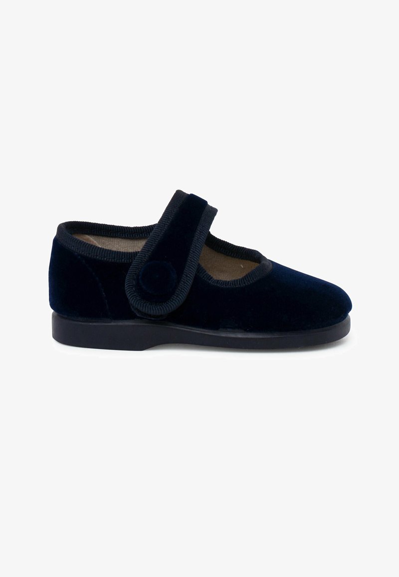 Zapato de terciopelo azul marino con puntera redondeada, suela negra plana y una amplia correa de velcro con un acento circular. Textura suave con un detalle mínimo.