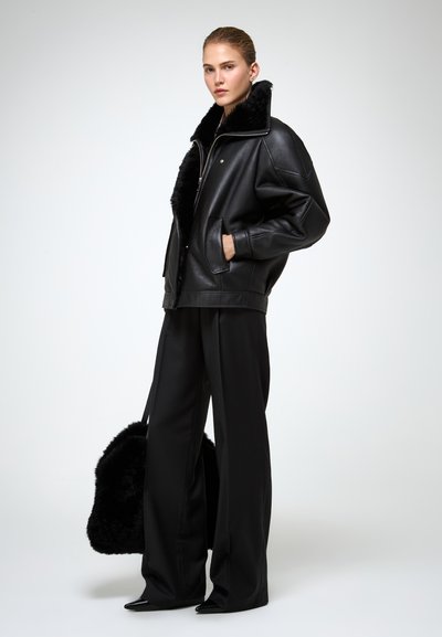 Zwarte leren jas met faux fur kraag, ritssluiting en zijzakken, gecombineerd met zwarte wijde broek en puntige hakken.