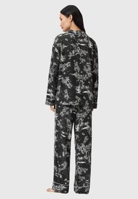 Czarny i biały zestaw piżamowy w kwiatowy wzór, składający się z luźnej koszuli i spodni w szerokim kroju z białymi lamówkami na brzegach.
