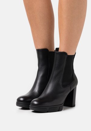 Las botas de tobillo de cuero negro presentan un diseño elegante, paneles laterales elásticos, un tacón grueso y un acabado texturizado, aptas para diversos conjuntos.