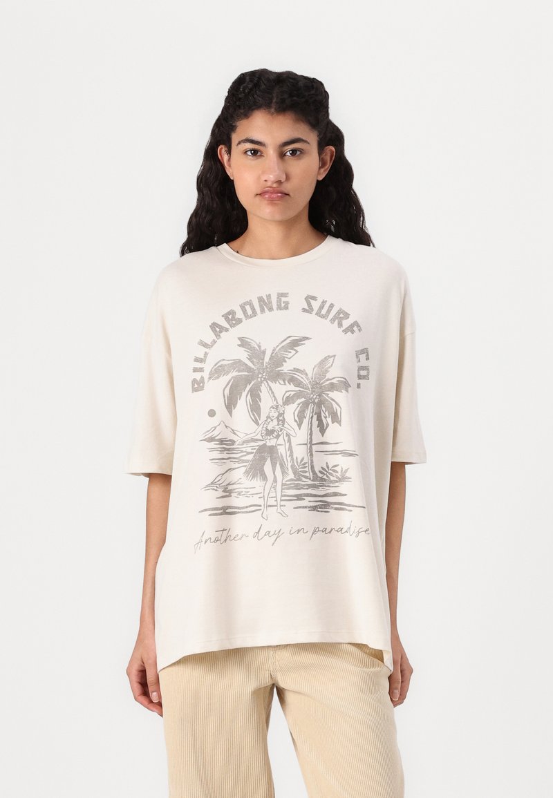 T-shirt oversize beige clair en coton, agrémenté d'un graphique vintage représentant un palmier et une danseuse hula en gris, avec un col rond et des manches courtes.