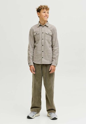 Chemise tissée marron clair avec deux poches poitrine, fermeture à boutons sur le devant et col, assortie à un pantalon en velours côtelé vert ample et des baskets grises.